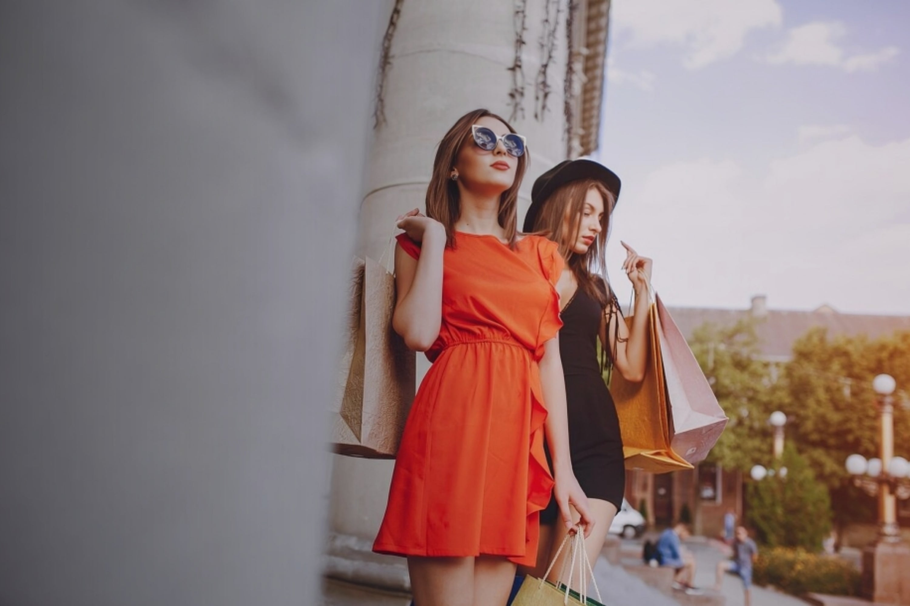 Two women walking outdoors with shopping bags, one in a red dress.