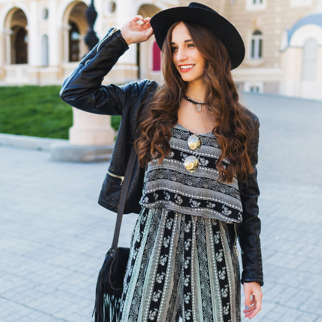 Woman in a stylish outfit with a black hat and patterned dress standing outdoors.