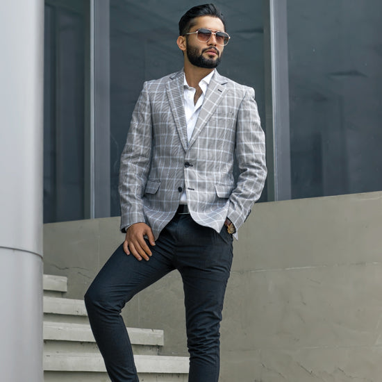 Man in a checkered blazer and sunglasses standing on steps with a modern building in the background