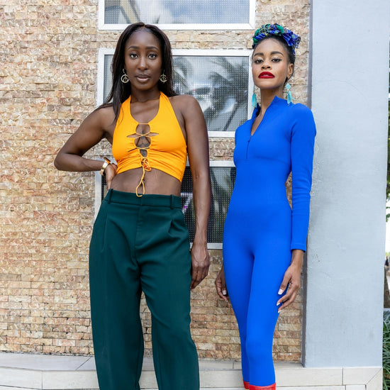 Two women in colorful outfits standing against a brick wall.