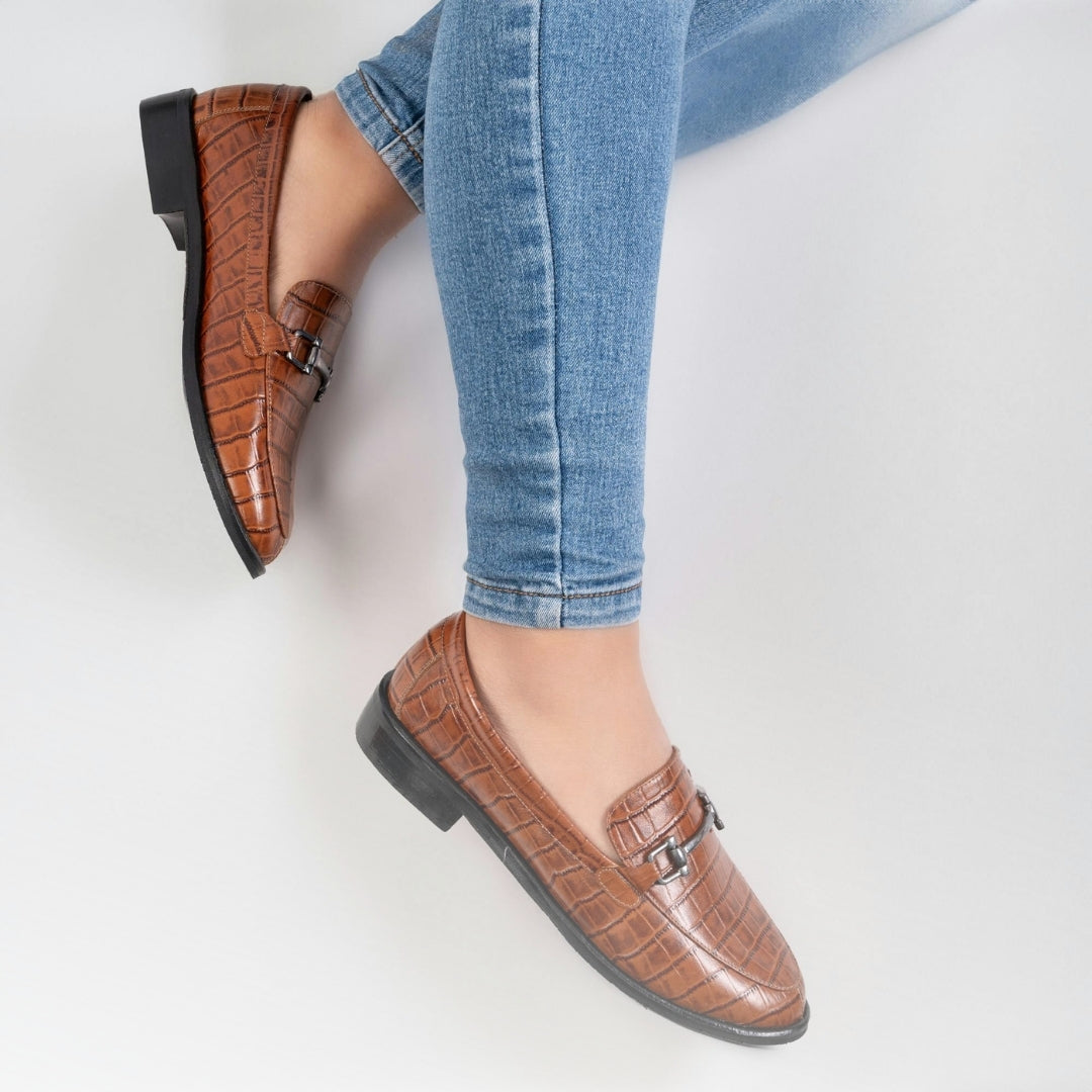 Brown loafers worn with blue jeans on a light gray background